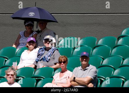 Les spectateurs s'assoient sous un parapluie pour se protéger du soleil en regardant Gustavo Fernandez en action contre Alfie Hewett lors de leur demi-finale de match des célibataires en fauteuil roulant pour hommes le 12 e jour des Championnats de Wimbledon 2022 au All England Lawn tennis and Croquet Club, Wimbledon. Date de la photo: Vendredi 8 juillet 2022. Banque D'Images