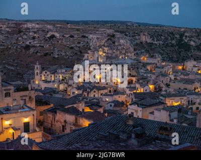 Vue panoramique en soirée de la sassi ou de la vieille ville de Matera, Basilicate, Italie avec une église et des maisons troglodytes quand les lumières du soir s'allument Banque D'Images