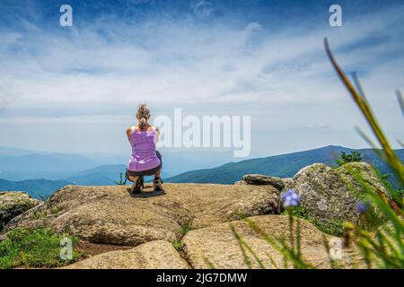 Vue arrière d'une femme de randonnée qui s'accroupille sur un rocher dans les Blue Ridge Mountains par une journée ensoleillée. Banque D'Images