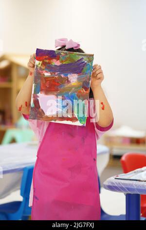 Une petite fille tenant la paix de l'art, enfants peinture désordonnée des arts de peinture et de l'artisanat portant un tablier rose. Banque D'Images