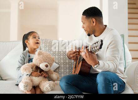 Pouvez-vous chanter. Prise de vue d'un jeune père jouant de la guitare pour sa fille à la maison. Banque D'Images