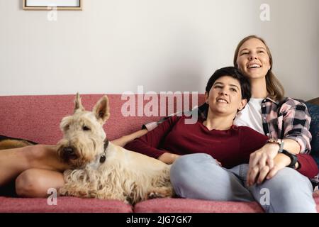 Femme caucasienne couchée sur l'épaule d'une petite amie heureuse tout en se relaxant avec un terrier écossais sur le canapé Banque D'Images