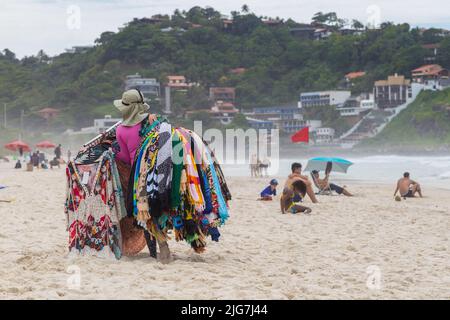 BARRA DA TIJUCA, RIO DE JANEIRO, BRÉSIL - 2 JANVIER 2020: Vendeur de plage typique brésilienne marchant sur la plage et portant pour la vente des robes. Banque D'Images