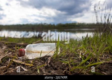 Déchets abandonnés sur la nature. Dommages causés à l'environnement par la pollution des déchets humains. Bouteille en plastique gauche au milieu de l'herbe sur la rive de la rivière Banque D'Images