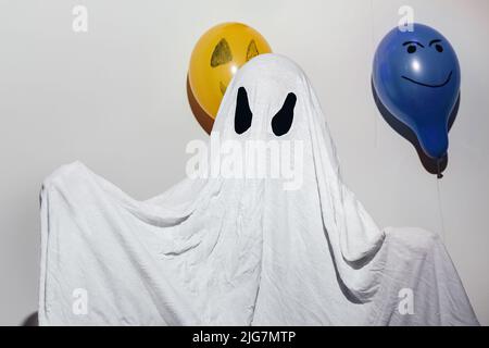 Joyeux Halloween. Un enfant dans un costume fantôme blanc fait maison et peint des boules orange et bleu. Yeux en papier. Design festif, concept de fête. Fête de la Toussaint. Banque D'Images