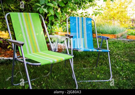 Deux chaises pliantes de jardin se tiennent à l'ombre sous un arbre lors d'une chaude journée d'été dans le jardin, en gros plan. Banque D'Images