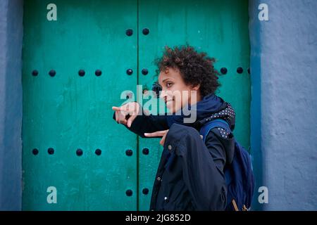 Femme afro-américaine pointant du doigt avec un regard souriant près de la porte verte Banque D'Images