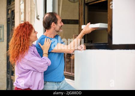 Un couple d'âge mûr reçoit une boîte à pizza avec ses restes dans un restaurant. Banque D'Images