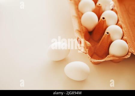 Les œufs de poulet blancs sont dans un emballage en carton orange du magasin, se tenant sur une table blanche, et deux œufs sont couchés à côté. Breakfas aux protéines saines Banque D'Images