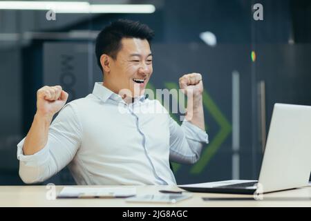 Homme d'affaires asiatique travaille dans un bureau moderne, se réjouit à la fin de la journée de travail, et est satisfait du travail fait, l'homme regarde les ordinateurs portables s. Banque D'Images