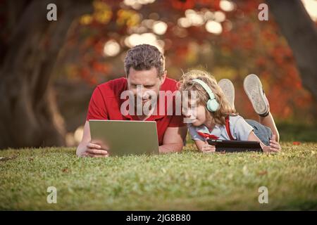 une famille heureuse de papa et de fils utilise un ordinateur portable et des écouteurs dans le parc, week-end familial. Banque D'Images