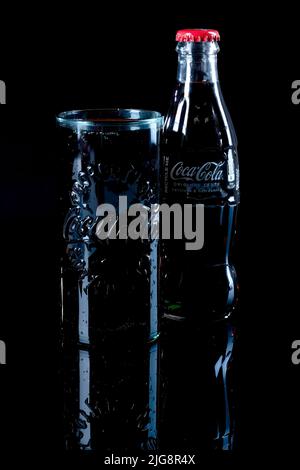 Un verre plein de Coca Cola à côté d'une bouteille sur une surface réfléchie Banque D'Images