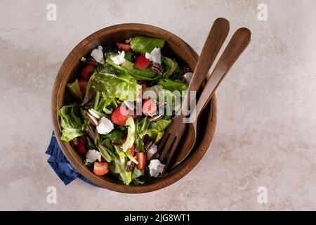 Un fond texturé vert olive rustique avec une salade saine dans un bol en bois avec mélange de printemps, fraises, bleuets, pacanes et fromage de chèvre et Banque D'Images