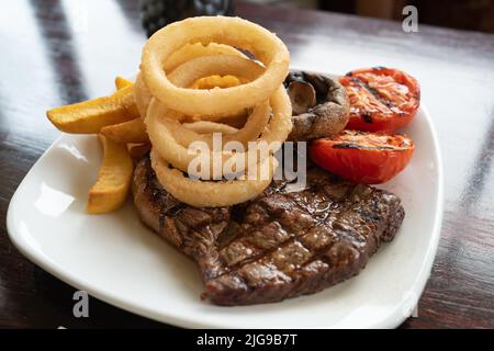 Peu profond foyer sur les rondelles d'oignon battues sur une assiette avec un steak et des chips avec des tomates et des champignons. Banque D'Images