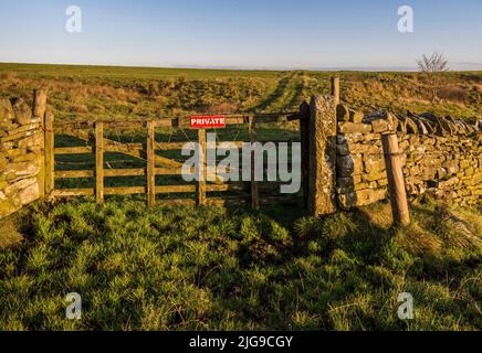 Porte avec panneau « privé » et fil barbelé empêchant l'accès d'une chaussée publique vers le nord à une voie traversant une ferme ouverte de Northumberland, en Angleterre Banque D'Images