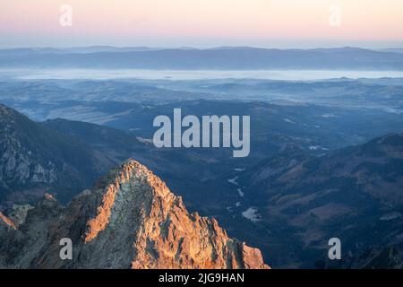 Pic proéminent qui attrape la lumière du lever du soleil avec chaîne de montagnes et vallée brumeuse en arrière-plan Banque D'Images