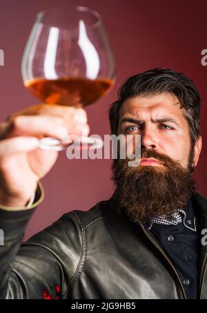 Homme barbu avec un verre de whisky ou de brandy. Boisson alcoolisée. Dégustation, dégustation. Fête, vacances. Banque D'Images