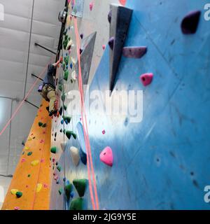 Jeune homme grimpant sur un mur d'escalade intérieur vu d'en-dessous ; cordes et cales d'escalade pour le soutien de l'ascension. Banque D'Images