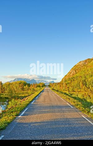 Vue sur une route et une végétation verte menant à une zone isolée idyllique en été. De grands arbres verts entourant une rue vide à la campagne Banque D'Images