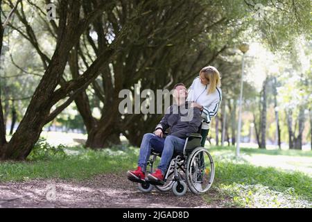 Femme marchant avec un homme handicapé en fauteuil roulant dans le parc Banque D'Images