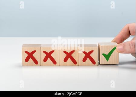 Man Hand sélectionne une case à cocher avec une coche verte dans une rangée de plusieurs cases avec des croix rouges. Pro et contra ou accepter et refuser. Stratégie de choix. Banque D'Images