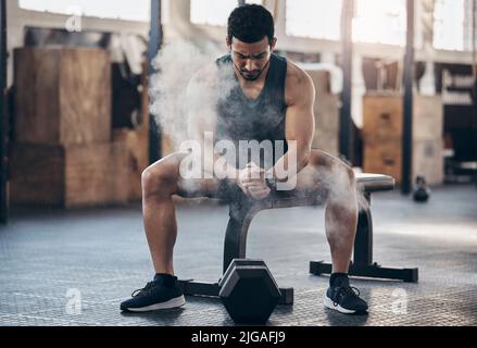 Je suis prêt à gronder. Un jeune homme musclé se dépoussiérant les mains avec de la poudre de craie tout en faisant de l'exercice avec une haltère dans une salle de gym. Banque D'Images