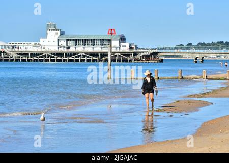 Bournemouth, Dorset, Angleterre, Royaume-Uni, 9th juillet 2022, Météo. Onde de chaleur. Les gens arrivent à la plage avant 9 heures le samedi matin. Les températures atteindront la température élevée de 20s par après-midi sous le soleil de mur à mur. Femme marchant sur la plage. Crédit : Paul Biggins/Alamy Live News Banque D'Images