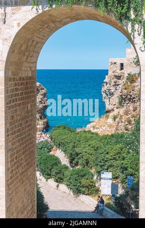 Belle vue de Polignano a Mare avec maisons en pierre blanche, falaise, plage, mer bleue et touristes, baigneurs, entouré par la nature méditerranéenne Banque D'Images