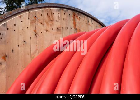 Bobine en bois de câble électrique rouge à l'extérieur au ciel bleu ciel nuageux. Concentrez-vous sur le troisième câble en partant de la droite Banque D'Images