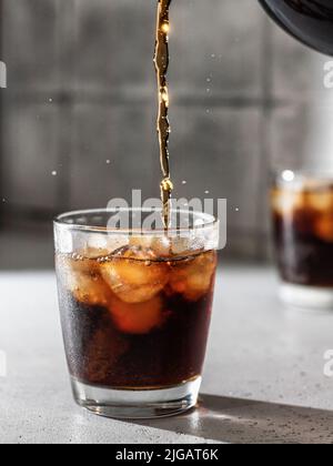 Verser le Cola ou le cocktail Cuba libre dans un verre avec des glaçons. Boisson non alcoolisée avec éclaboussures. Orientation verticale Banque D'Images