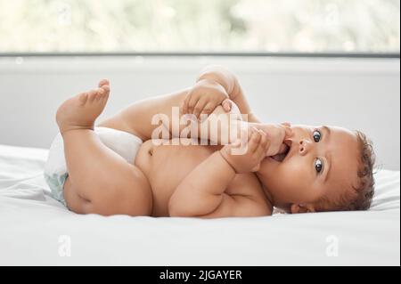 MMM... orteils. Un adorable bébé garçon allongé sur le lit et jouant avec ses pieds à la maison. Banque D'Images