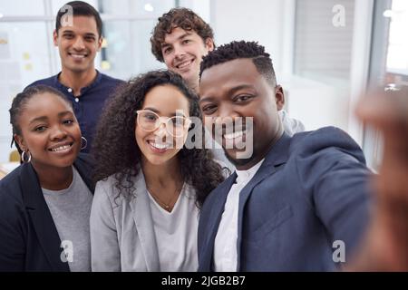 Nous capturer dans notre plus haut moment de réussite. Un groupe diversifié d'hommes d'affaires debout au bureau et prenant un selfie. Banque D'Images