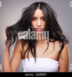 Je suis officiellement en guerre avec mes cheveux. Une jeune femme attrayante debout seule dans le studio et se sentant frustrée en regardant ses cheveux. Banque D'Images