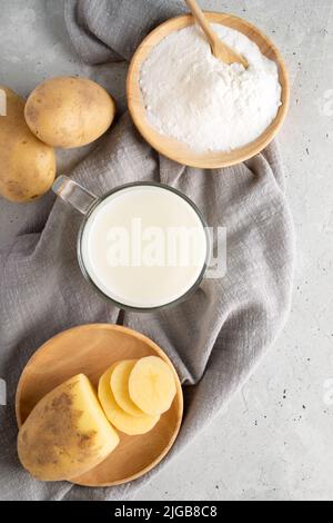 Verre de lait en poudre de pomme de terre, assiette en bois avec poudre de pomme de terre, tubercules sur serviette grise sur béton. Lait végétalien sans lactose à partir de poudre. Base de l'usine Banque D'Images