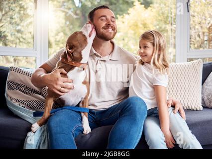 On peut dire sans risque que Dads est le favori ici. Un beau jeune homme assis sur le canapé à la maison et se liant avec sa fille et son chien. Banque D'Images