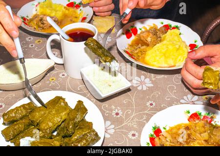 La famille mange à la table du dîner. Dolma sur un plateau, sauce et purée de pommes de terre au chou, mugs avec boissons, vue de dessus. Banque D'Images