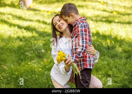 Petit garçon mignon embrassant la mère et donnant des fleurs. Femme qui reçoit des pissenlits et qui embrasse un enfant. Banque D'Images