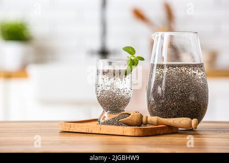 Verre d'eau, carafe, pelle et planche avec graines de chia sur la table dans la cuisine Banque D'Images