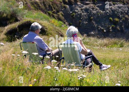 Couple senior assis sur des chaises de jardin en herbe, île de Valentia, Kerry, Irlande Banque D'Images