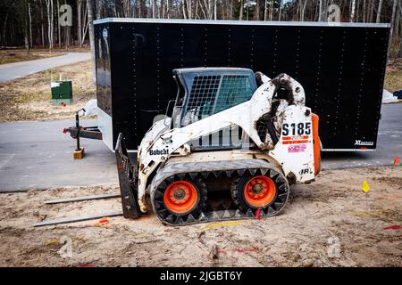 CROW WING CO, MN - 5 MAI 2022 : Bobcat avec chariot élévateur sur terre et une remorque à revêtement noir sur la chaussée. Banque D'Images