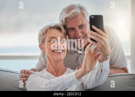 Faites en sorte qu'ils gardent beaucoup de souvenirs. Un couple affectueux et expérimenté qui prend des selfies tout en se relaxant dans le salon à la maison. Banque D'Images