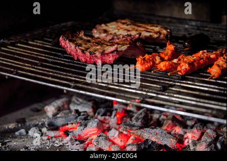 Côtes de porc et brochettes de poulet marinées cuisant au charbon de bois sur une grille de barbecue Banque D'Images