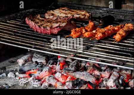 Côtes de porc et brochettes de poulet marinées cuisant au charbon de bois sur une grille de barbecue Banque D'Images