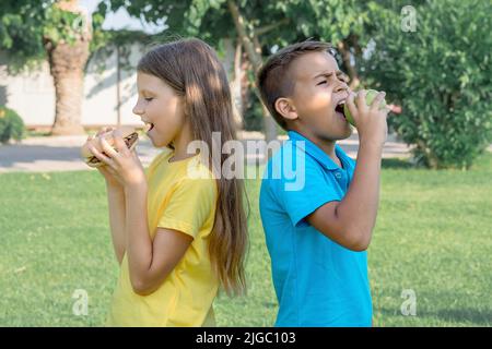 Les écoliers mangent des hamburgers dans le parc. Déjeuner après l'école. Banque D'Images