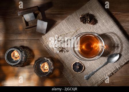Vue en hauteur d'une belle tasse de verre de thé chaud sur une table en bois avec fleurs séchées, citron sec et bougies apaisantes Banque D'Images
