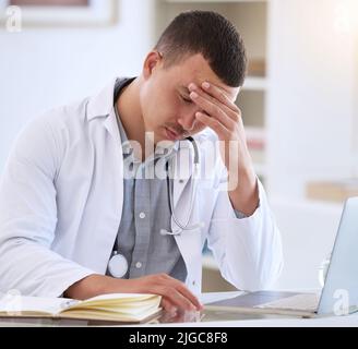 Je n'aurais pas pu avoir de pire nouvelles. Un jeune médecin charmant assis seul dans sa clinique et se sentant stressé en utilisant son ordinateur portable. Banque D'Images