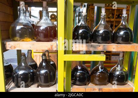 étagère en bois jaune avec différentes carafes de bouteilles de verre bulbous remplies de vinaigre et de vin placé devant la stalle sur un marché Banque D'Images