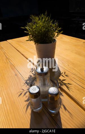 Gros plan sur une table de bar en bois en plein air avec sel de sucre et poivre comme croûtes devant une plante verte en métal argenté stand contre le soir s. Banque D'Images