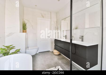 Intérieur moderne et élégant salle de bains design intérieur avec toilettes et baignoire blanches, lavabos et un grand miroir au-dessus de la salle de bains lumineuse avec toilettes Banque D'Images