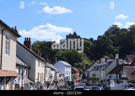 La rue animée de Dunster dans le Somerset lors d'une belle journée ensoleillée est surplombante par le magnifique château de Dunster. Il s'agit d'une propriété de National Trust Banque D'Images